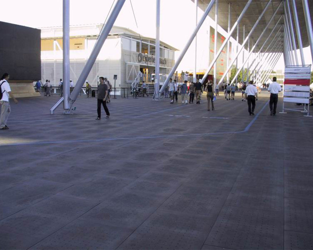 People walking on a temporary surface protection in an outdoor area with modern architecture.