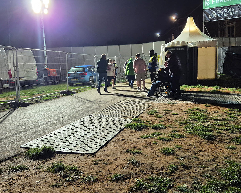 People walking near a car with a mat on the ground at night.