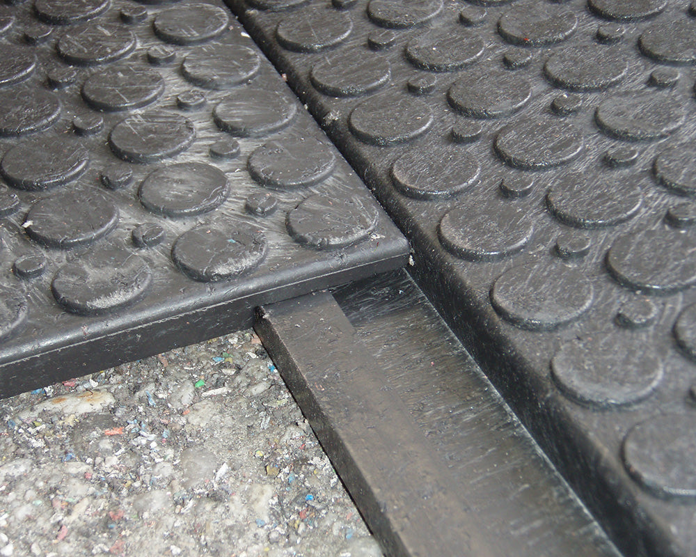 Close-up of two black rubber mats with textured surface on a concrete floor.