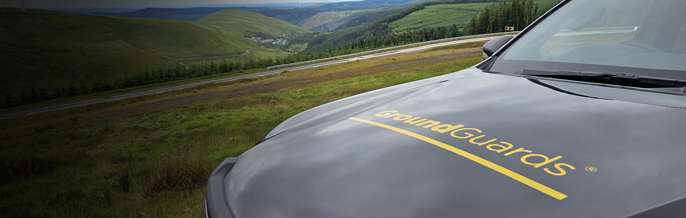 Car hood with 'GroundGuards' branding on a scenic road background