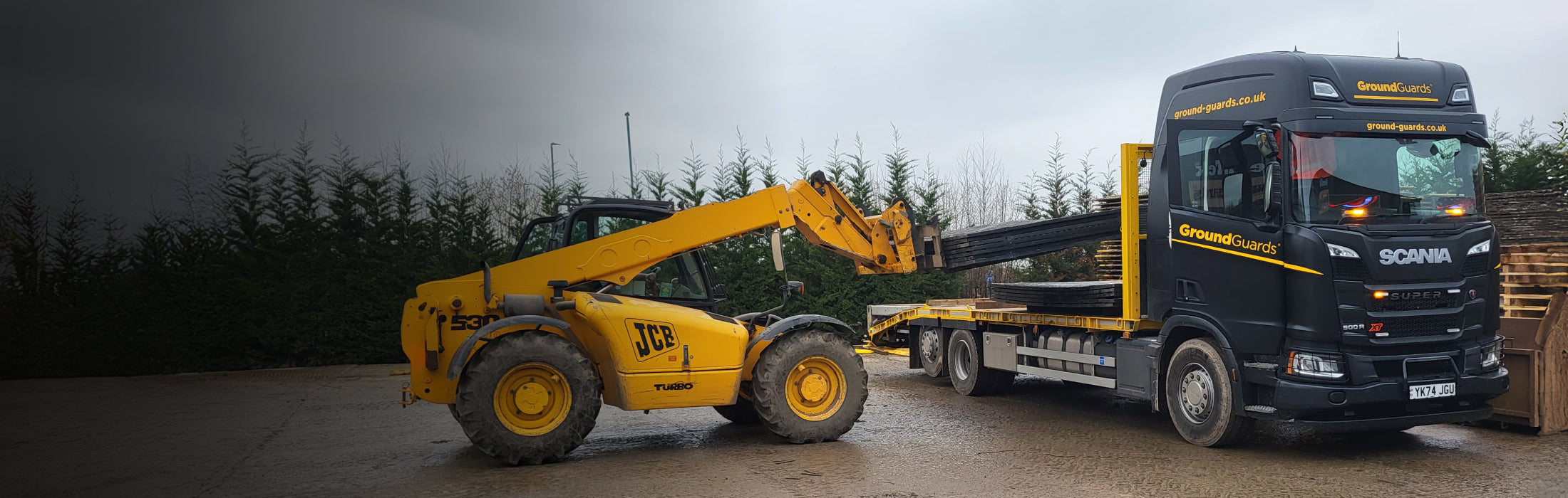 Scania truck being loaded by a yellow telescopic handler with ground protection mats.