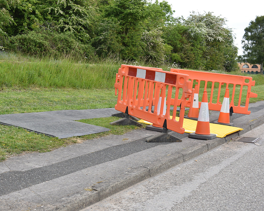 Orange barriers and traffic cones on a road with greenery in the background