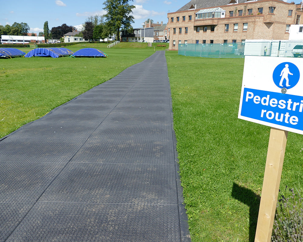 Temporary path leading to a building with a 'Pedestrian route' sign on grass.