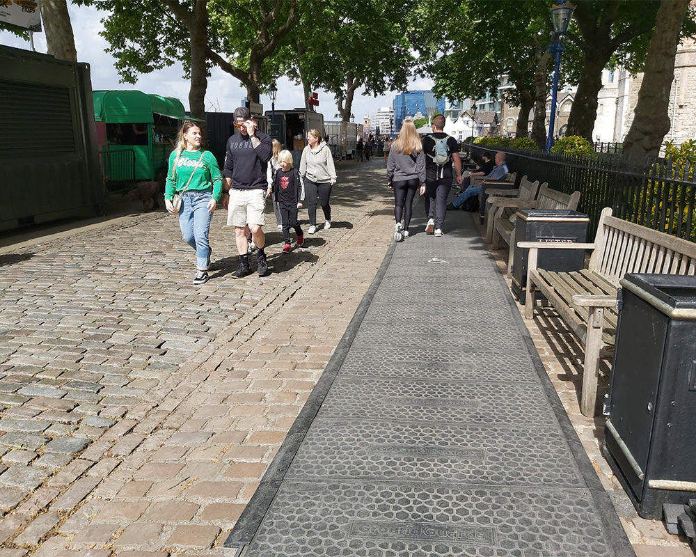 People walking on a paved path next to a building with a green awning.