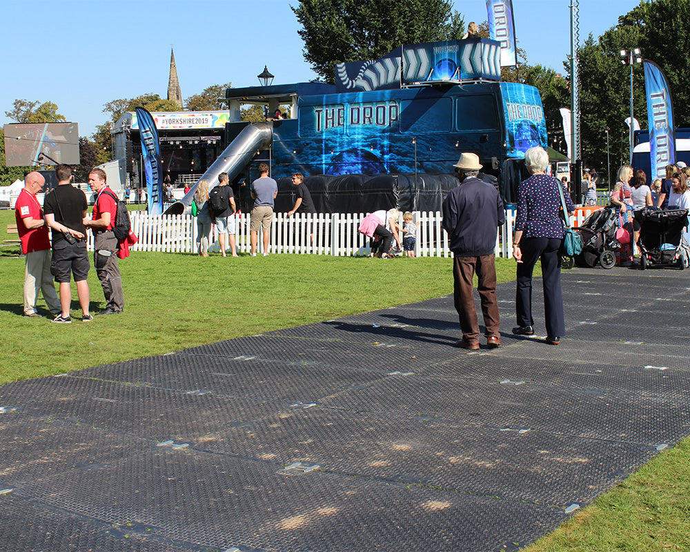 Event with people gathered around a large blue and black structure labeled 'The Drop' on a grassy area.