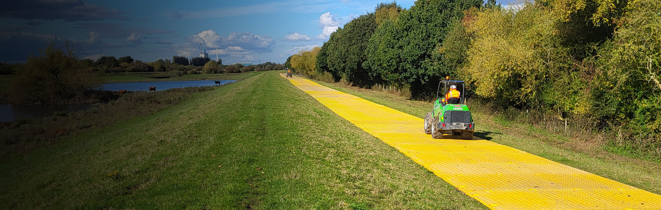 Loader on a yellow haul road made from XtremeMat, next to a grassy area with trees under a blue sky.