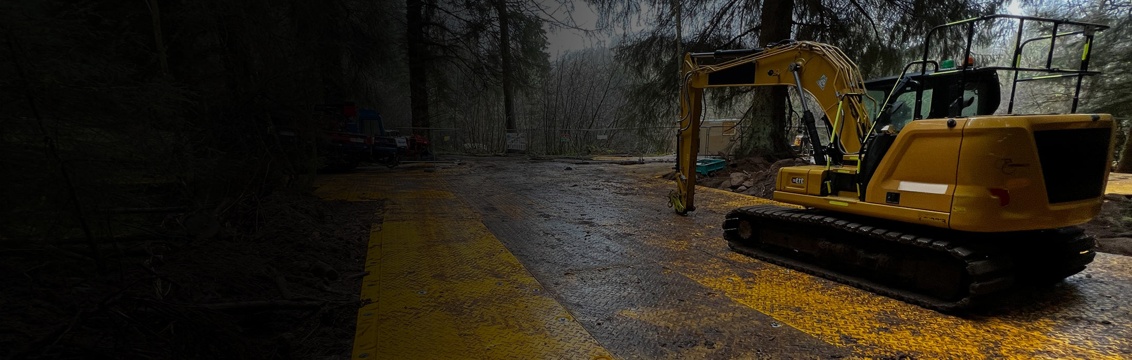 Yellow excavator on temporary work platform made using XtremeMats on site with trees in the background