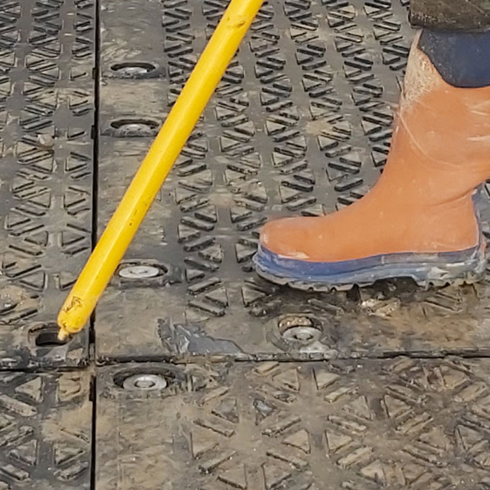 Person wearing orange boots stepping onto a metal platform with a yellow tool.