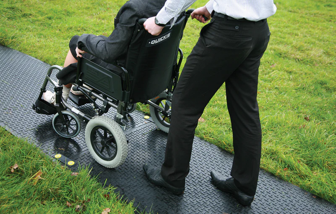 Wheelchair using temporary access mats across grass and soft ground